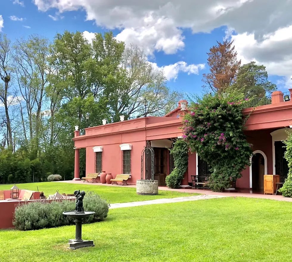 The main house at Estancia La Loma seen across the lawn, with a stone fountain and the sunken fire pit in front of it