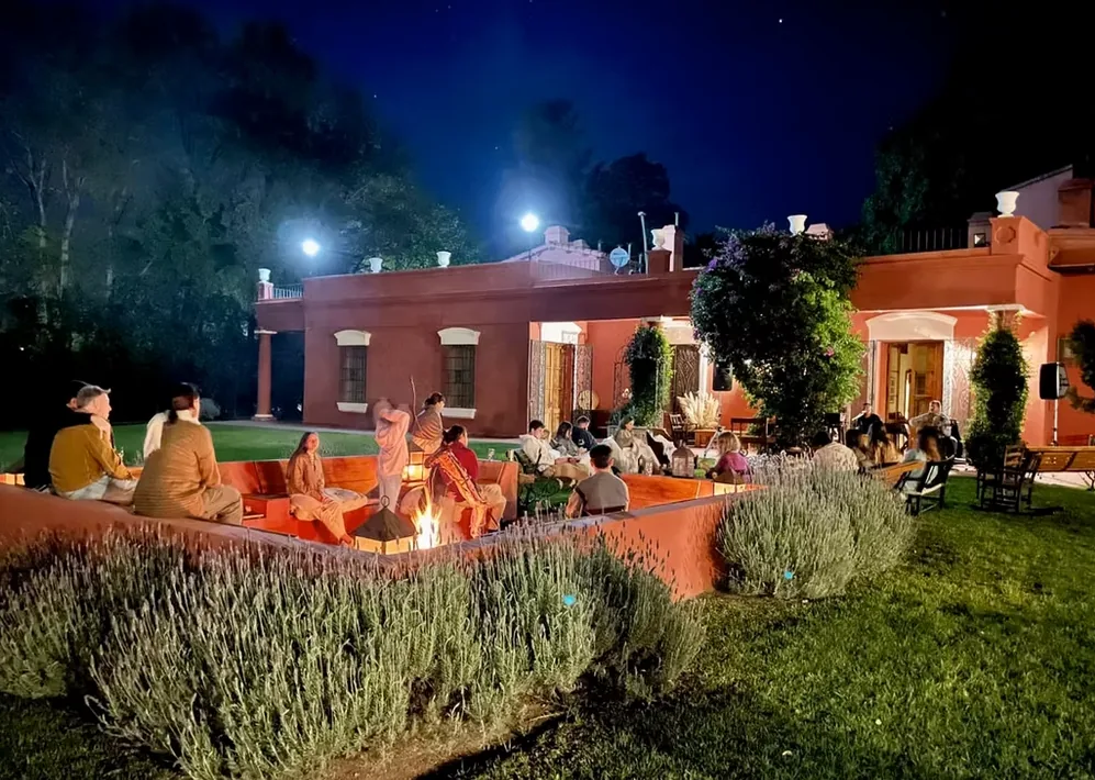 People sitting around the lit fire pit at Estancia La Loma at night, with the house behind them