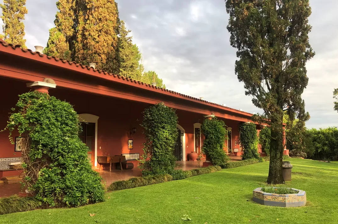La galerie à colonnes de la maison principale de l'Estancia La Loma en fin de journée, avec la pelouse et les vieux arbres devant