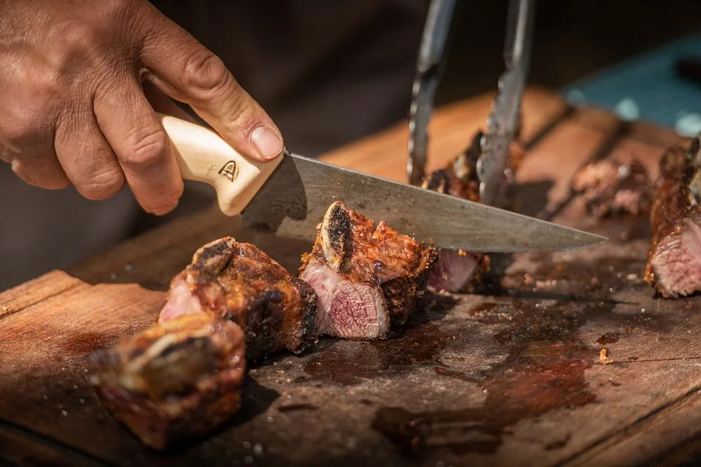 Grilled ribs being carved on a wooden board at Río de Piedras