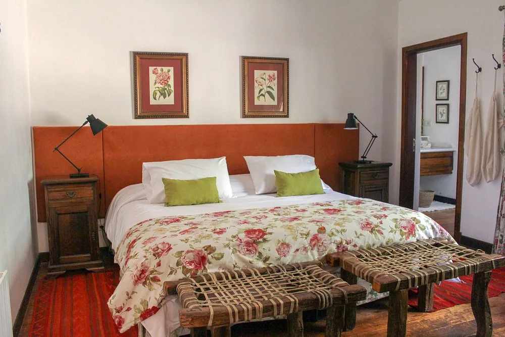 A bedroom at Río de Piedras with a double bed, botanical prints above it and the private bathroom through the door
