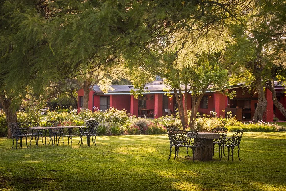 Wrought-iron tables set out on the lawn at Río de Piedras, with the house and its flower beds behind